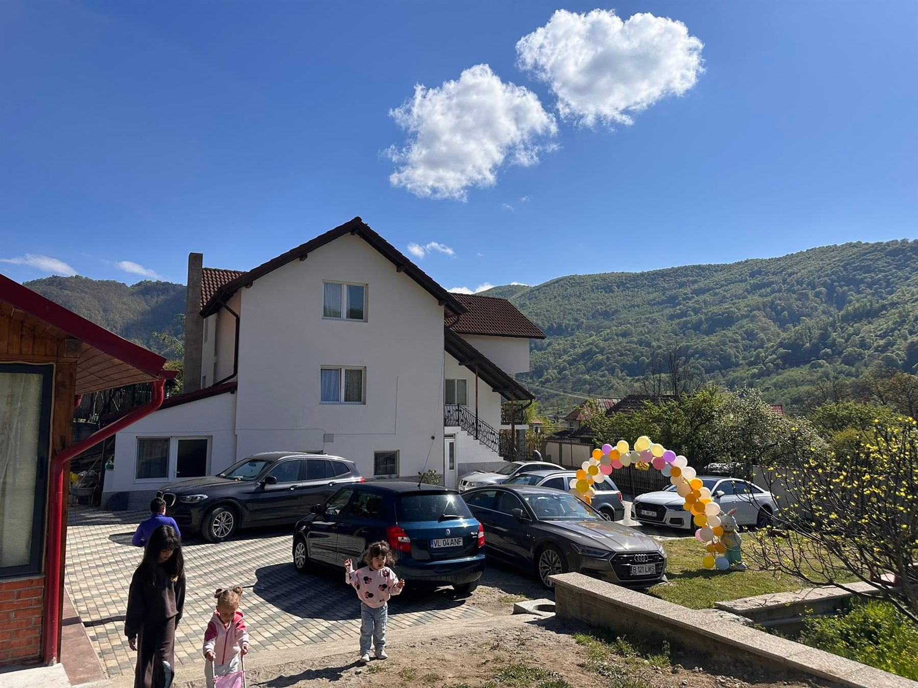 Curtea Casei Ioana în timpul unei aniversări, cu arcadă de baloane și mașinile grupului parcate
